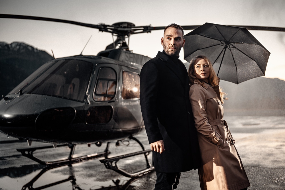 Mann und Frau unter schwarzem Regenshchirm vor Hubschrauber